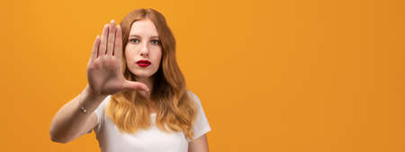 Young pretty woman with wavy redhead, looking serious and stern, wearing white t-shirt, showing open...