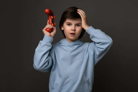 Unhappy boy 10-12 years old, dressed in casual clothes, standing with joystick and holding his hand on his head. OH, NO, I didn't win. Childhood, Human emotions, facial expression concept.の写真素材