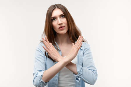 Serious girl with long chestnut hair, dressed in casual clothes, gesturing stop, finish, symbol of rejection, not allow violence, body language. Human emotions, facial expression concept.の写真素材