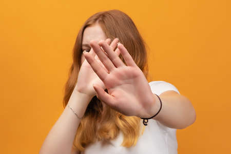 Pretty girl with wavy redhead, wearing white t-shirt covering eyes with hands and doing STOP...