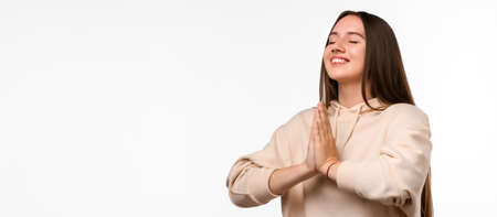 Image of pleased brunette woman with long hair smiling and holding palms together dressed in casual...
