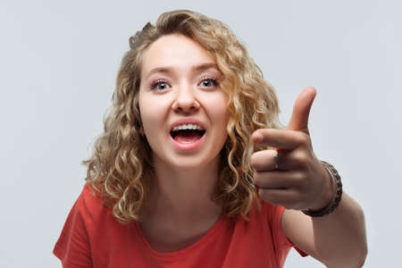 Pretty Young woman with curly hair in casual t shirt looking at the camera and pointing her finger...