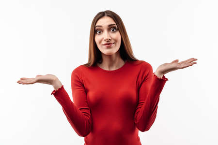 I don't know. Young shocked woman with long chestnut hair, wearing in casual red sweater expressing surprise on camera, spreads hands with aside. Concept of doubt, uncertainty and confusionの写真素材