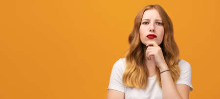 Photo of Pensive young woman with wavy redhead standing with hand raised on chin and looking...