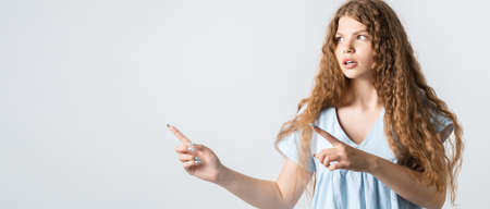 You better see it. Intrigued European girl with curly long hair, points away with both for fingers, shows blank space for your promotion. People, advertisement conceptの写真素材