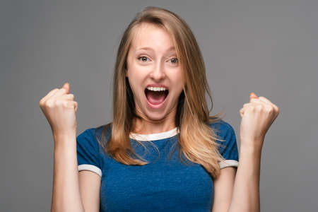 Successful Young female with blonde straight hair, dressed in blue t shirt, smiling happily,...