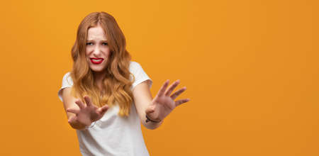 Pretty girl with long wavy blonde hair, wearing white t-shirt, standing disgusted expression,...
