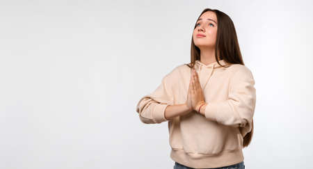 Image of pleased brunette woman with long hair smiling and holding palms together dressed in casual clothes. She meditating, praying for peace and love, having calm and peaceful facial expressionの写真素材
