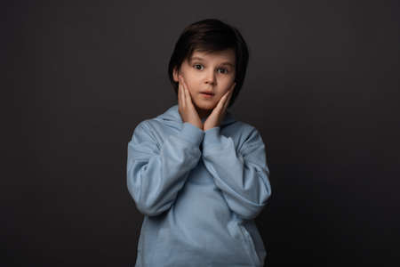 Image of shocked boy 10-12 years old, dressed in casual clothes expressing surprise on camera. Studio shot, gray background. Human emotions, facial expression conceptの写真素材