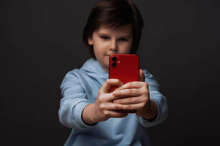 Image of Cute boy 10-12 years old, dressed in casual clothes using smartphone. Image with selective focus on smartphone. Studio shot, gray backgroundの写真素材