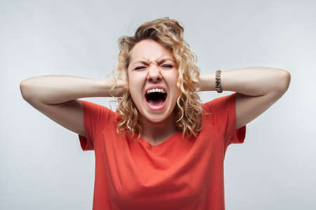Image of stressed blonde girl with curly hair in casual t shirt grabbing her head. Emotional helplessness. Problems, surprise, fear, fobia concept. Studio shot, white background.の写真素材