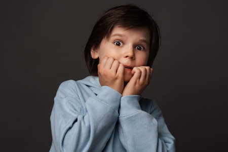 I'm afraid. Image of scared boy 10-12 years old in casual clothes covering his mouth with hands. Fright, phobia, panic attack, horror and facial expression concept. Studio shot, gray backgroundの写真素材