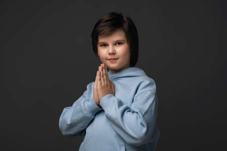 Portrait of boy 10-12 years old in casual clothes keeping palms together and praying. He meditating, praying for peace and love, having calm and peaceful facial expression. Facial expression conceptの写真素材