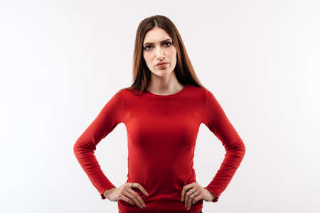 Portrait of irritated young woman with long chestnut hair in casual red sweater frowning and looking...