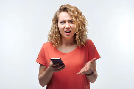 Young woman with curly hairstyle using mobile phone. New useful application, uses fast unlimited internet, makes shopping online. Studio shot, white background, isolatedの写真素材