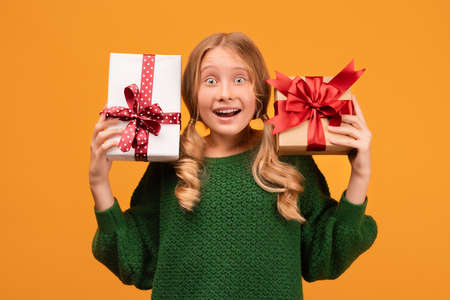 Image of charming blonde girl 12-14 years old in warm green sweater holding a lot of gift boxes....