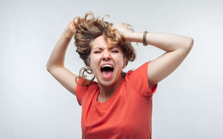 Image of stressed blonde girl with curly hair in casual t shirt grabbing her head. Emotional helplessness. Problems, surprise, fear, fobia concept. Studio shot, white background.の写真素材