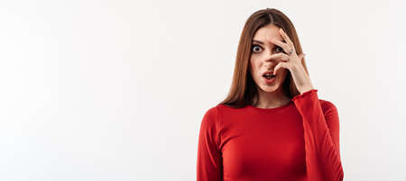 Portrait of frightened young woman with long chestnut hair in casual red sweater covering her eyes with hands. Human emotions, facial expression conceptの写真素材