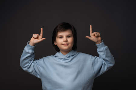 Portrait of Cute boy 10-12 years old in casual clothes pointing up with his index fingers, shows...