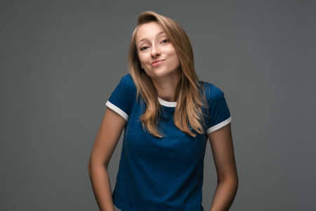 Studio shot of Good-looking woman with blonde straight hair wears blue t shirt, looks away enigmatically, wanting to do something illegally or secretlyの写真素材