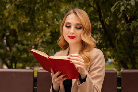 Charming young woman with long blonde hair reading book on the park bench. People lifestyle conceptの写真素材