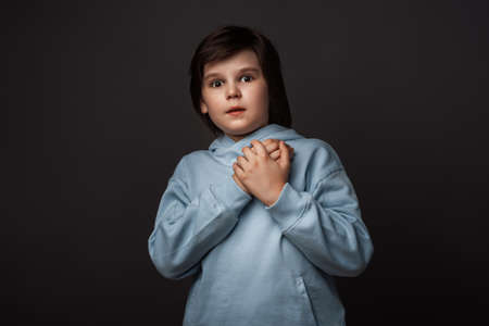 Image of shocked boy 10-12 years old, dressed in casual clothes expressing surprise on camera. Studio shot, gray background. Human emotions, facial expression conceptの写真素材