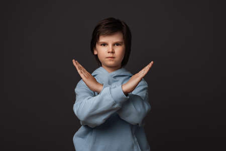 Image of serious boy 10-12 years old, dressed in casual clothes making X sign with crossed hands, gesturing stop, warning of danger. No way, stop doing. Human emotions conceptの写真素材