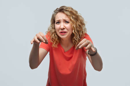 Image of dissatisfied blonde girl with curly hair in casual t shirt doing disgust face because aversion reaction with hands raised. Studio shot, white background. Facial expression conceptの写真素材