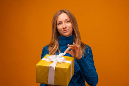 Portrait of a happy young woman in knitted blue sweater holding gift decorated with ribbon. Studio...