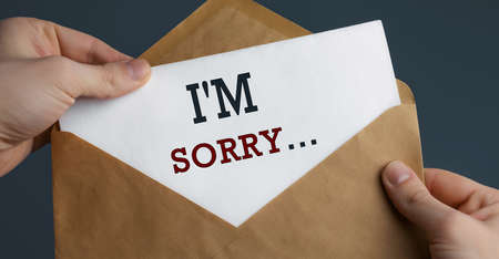 Male hands holding craft envelope with word SORRY on blue background, communication conceptの写真素材