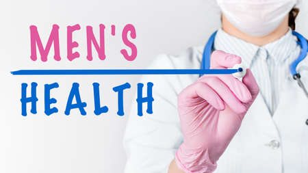 Close up female doctor in a white coat with stethoscope and pink sterile gloves writing text MEN'S HEALTH with marker. Medical conceptの写真素材