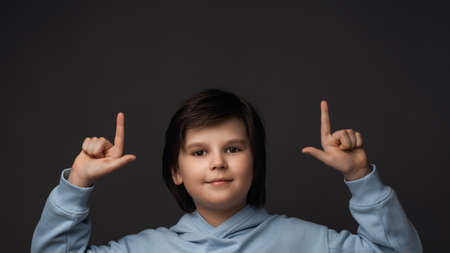 Portrait of Cute boy 10-12 years old in casual clothes pointing up with his index fingers, shows copy space for your information. Studio shot, gray background. Human emotions, facial expression conceptの写真素材