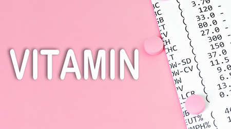 Word VITAMIN on pink background with a pills and financial documents, medical concept, top view