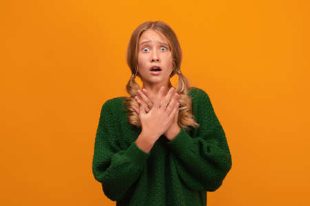 A blonde girl in warm green sweater expressing fear and horror.