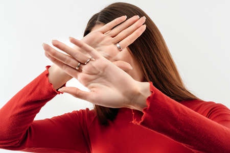Image of serious woman with long chestnut hair in casual red sweater gestures actively hands at camera, stop gesture with hands. No way, stop doing. Studio shot, white background. Human emotions conceptの写真素材