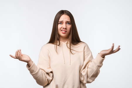 Studio shot of Insecure puzzled young female with long chestnut hair, spreads hands with doubt,...