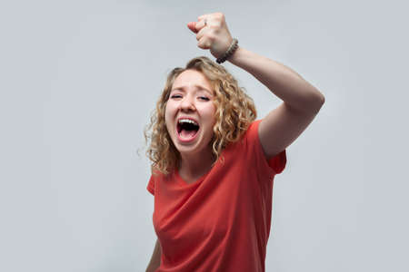 Image of young happy woman with curly hairstyle, dressed in casual t shirt smiling and making winner gesture, celebrating amazing news. Studio shot, white background, isolatedの写真素材