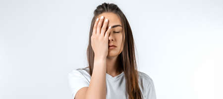 Young woman with long chestnut hair, covers face, closes eyes, feels fatigue, needs good rest, has...