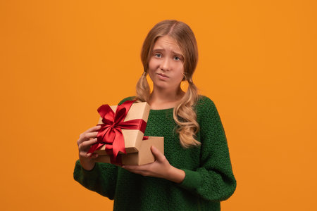 Charming blonde girl 12-14 years old in warm green sweater open a present box with red bow. Studio shot, yellow background, isolated. New Year Women's Day Birthday Holiday conceptの写真素材