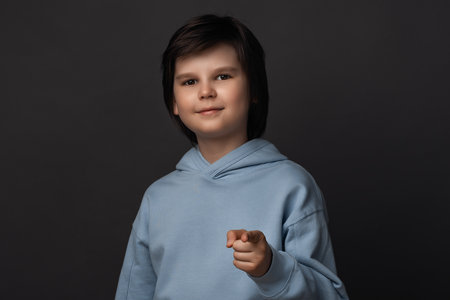 Photo of Cute boy 10-12 years old, dressed in casual clothes looking at the camera and pointing her finger at you. Studio shot, gray background. Human emotions, facial expression conceptの写真素材