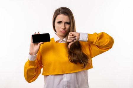 Pretty young brunette woman in casual clothes is showing smartphone blank screen in her hand. Girl don't recommend upload new app, online shopping site. Mock up copy spaceの写真素材