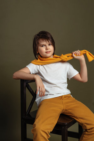 Handsome fashion young boy 11-13 years old sits on a chair in studio on green background. Casual style. Stylish shooting in studioの写真素材