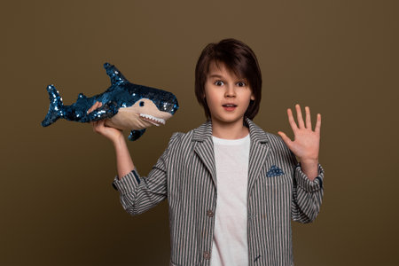 Portrait of young boy 11-13 years old posing with a toy shark in his hand in studio on green background. Casual style. Stylish shooting in studioの写真素材