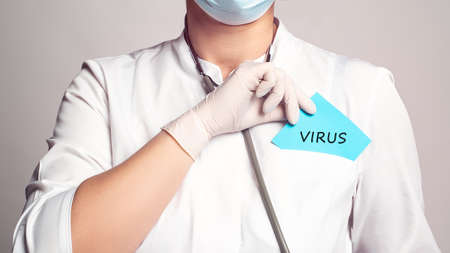 Cropped view of doctor in a white coat and sterile gloves holding a note with word - VIRUS. Medical conceptの写真素材