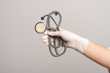 Closeup of the hand in a white sterile glove holding a stethoscope, isolated over gray background. Medicine, profession and healthcare conceptの写真素材