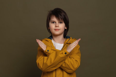 Serious little boy in casual clothes look keeping two arms crossed, denial concept. Studio shot, green backgroundの写真素材