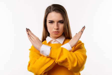 Serious Young brunette woman keeps two arms crossed, makes stop or ban gesture, indicates that the passage is closed, denial concept. Studio shot, white backgroundの写真素材