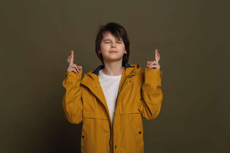 Waiting for a special moment. Portrait of dreamy little boy in casual clothes keeping his fingers...