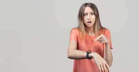 Too late, hurry up. Young beautiful blond woman in hurry pointing finger on wrist watch, impatience,...