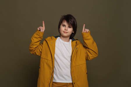 Your promo here. Portrait of attractive little boy in casual clothes pointing fingers up at...